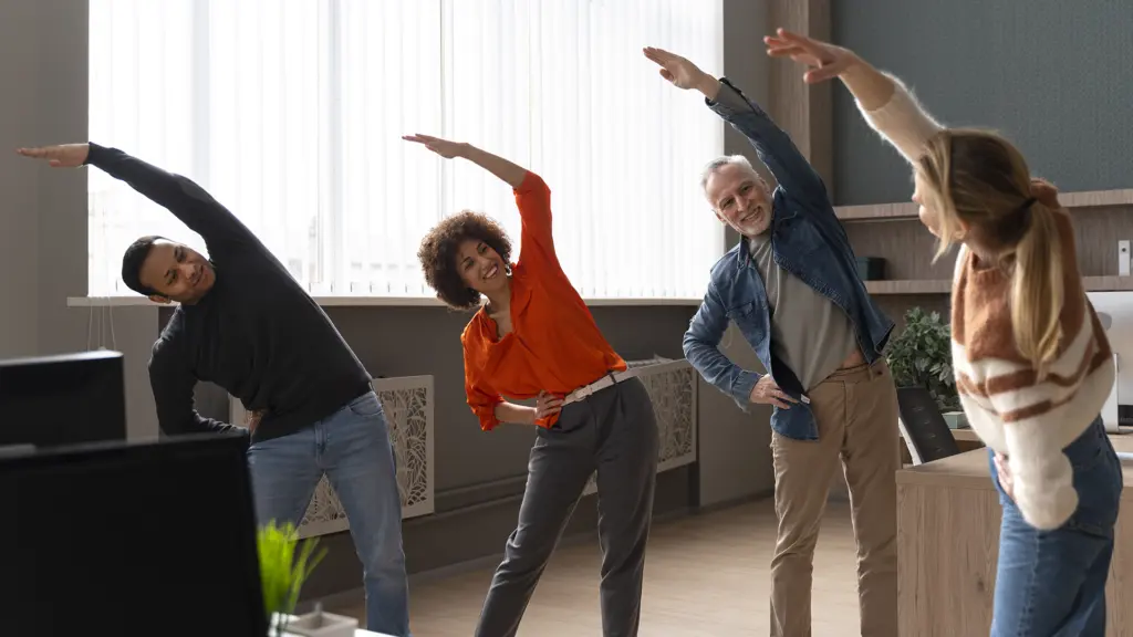 standing-office-yoga-workout-workout Vier Kolleginnen und Kollegen machen im Büro gemeinsam Dehnübungen