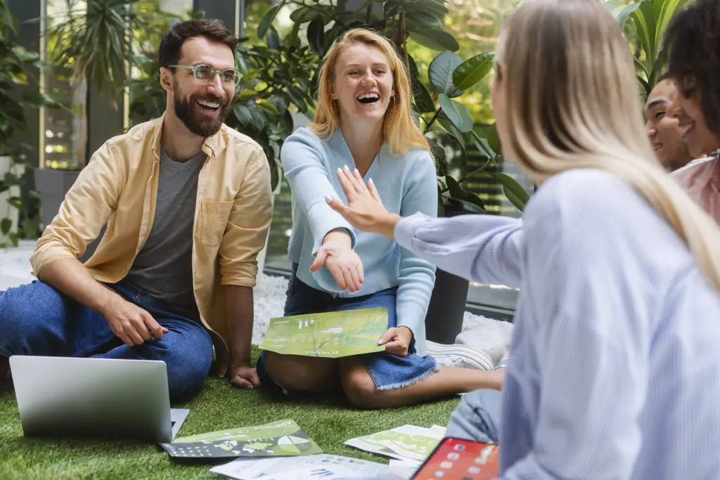 standing-office-yoga-workout-workout Team sitzt lachend im Freien auf dem Rasen zusammen, Gesundheitstag im Betrieb