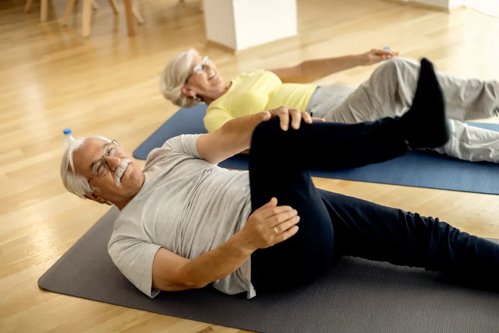 standing-office-yoga-workout-workout Älteres Paar macht Rückenübungen auf Gymnastikmatten in einer Halle