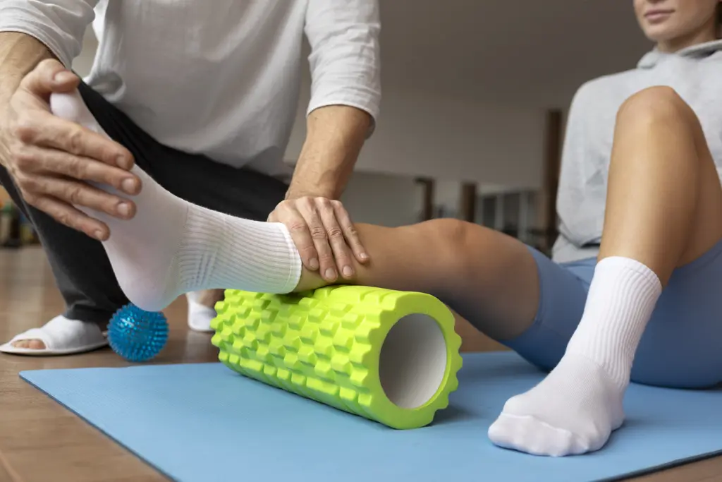 standing-office-yoga-workout-workout Trainer führt das Bein einer Person über eine Faszienrolle, Sportrehabilitation auf der Matte